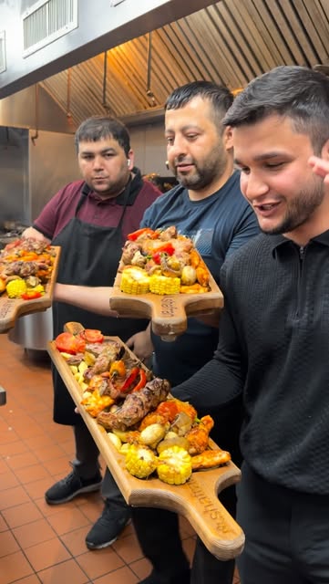 Staff carrying wooden boards of kebabs and grilled vegetables out of the kitchen